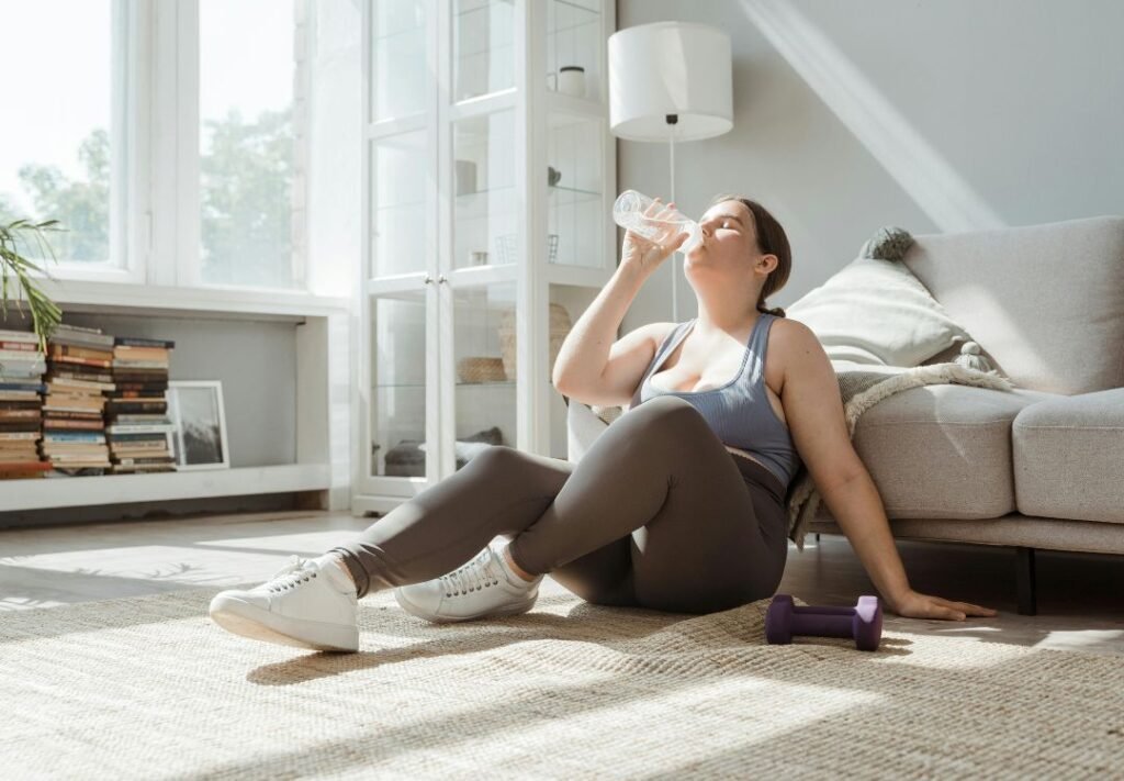 vida fitness em casa - mulher tomando agua na sala depois de realizar seu exercícios